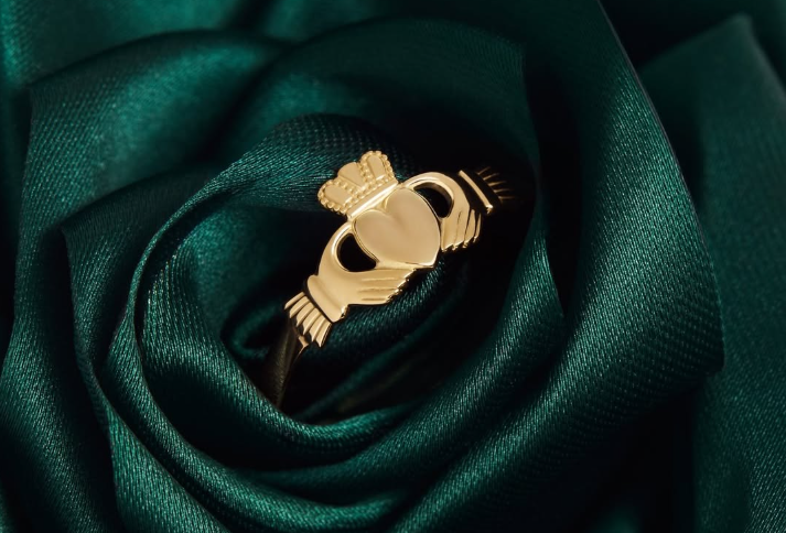 Gold claddagh ring on a dark green fabric background